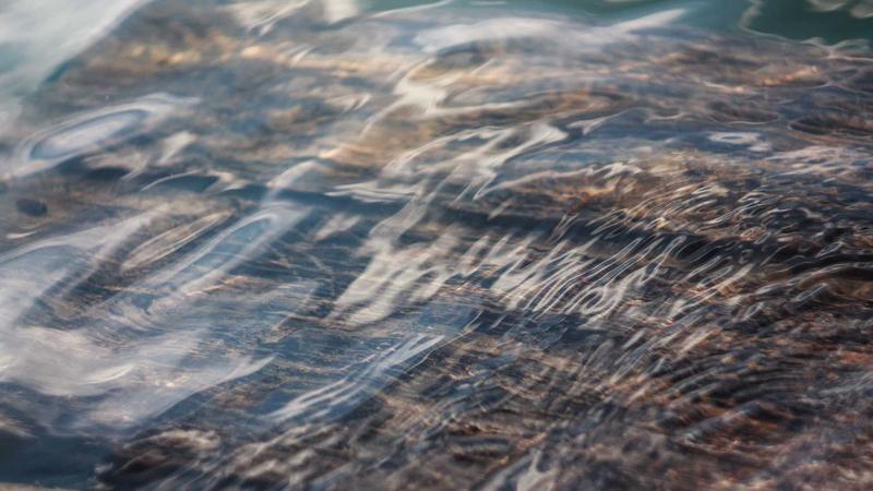 A modern, sleek smart battery charger plugged into a wall, charging four AA batteries with bright green LCD indicators, set on a wooden desk next to a gaming controller.