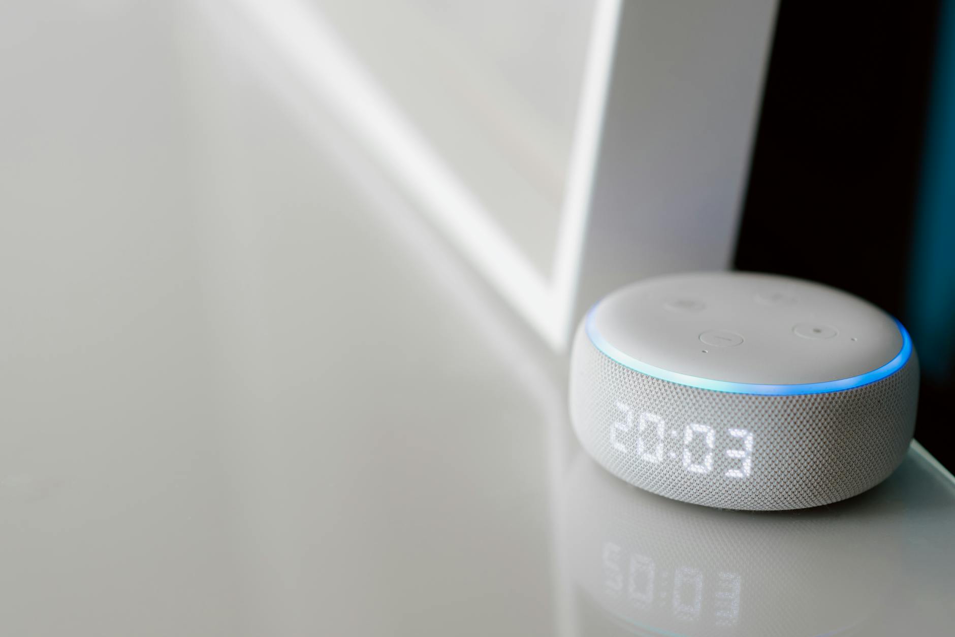 Close-up of a smart speaker with a digital clock display on a minimalist surface.