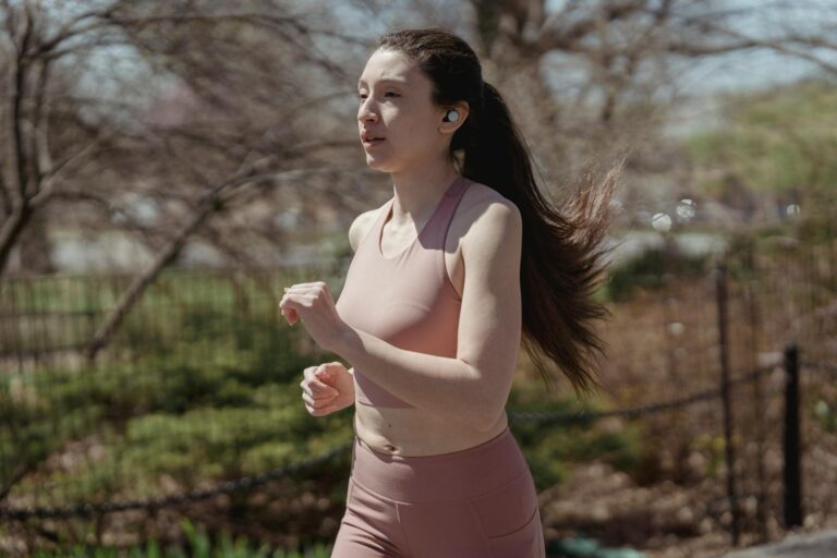 A woman jogs outdoors with wireless earbuds, embodying a healthy lifestyle.
