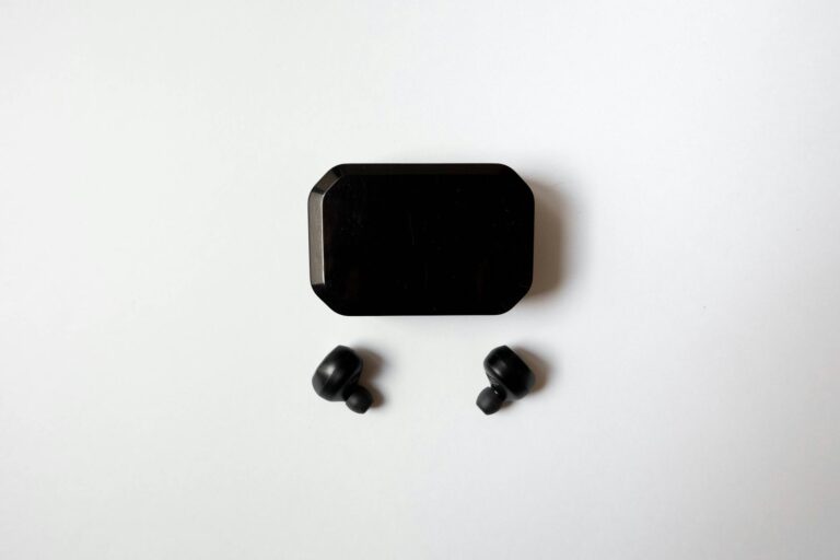 Top view of wireless earbuds with charging case on a white surface, showcasing sleek design and technology.