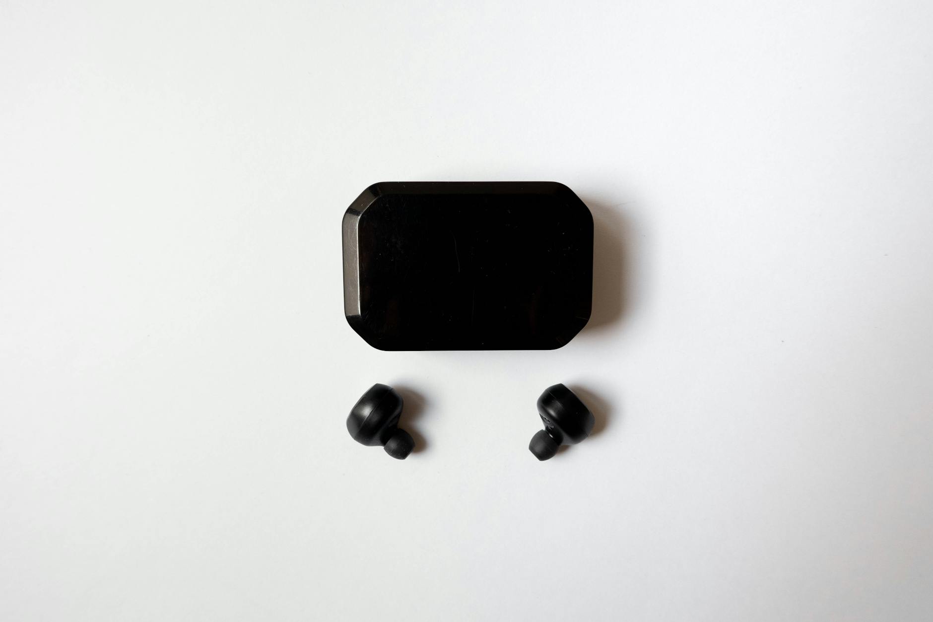 Top view of wireless earbuds with charging case on a white surface, showcasing sleek design and technology.