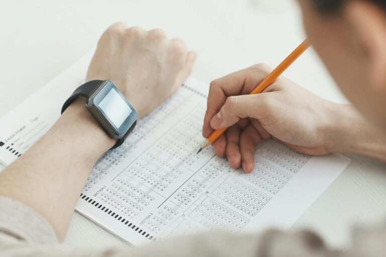 Close-up of a student writing answers on a test sheet with a pencil and smartwatch.
