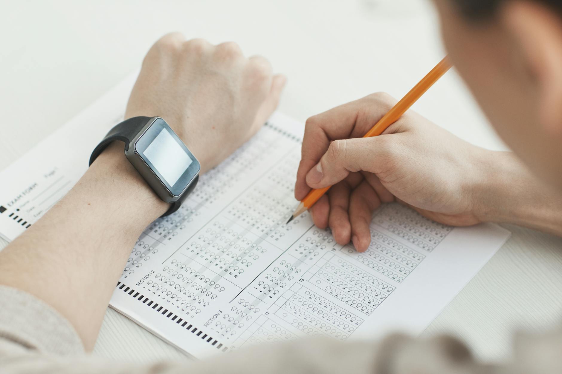 Close-up of a student writing answers on a test sheet with a pencil and smartwatch.