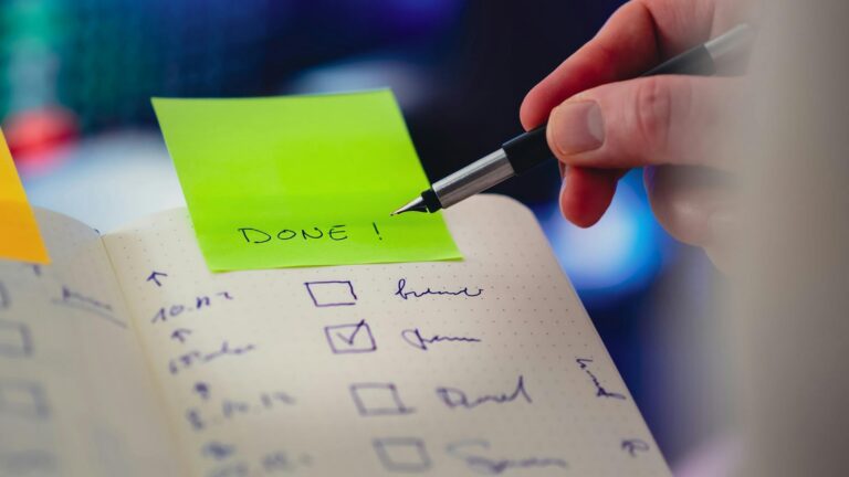 Close-up of a checklist and pen with brightly colored sticky note that says 'DONE!' indicating task completion.