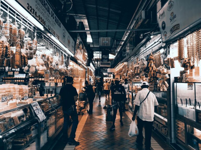 A bustling indoor market aisle filled with diverse shops and people shopping.