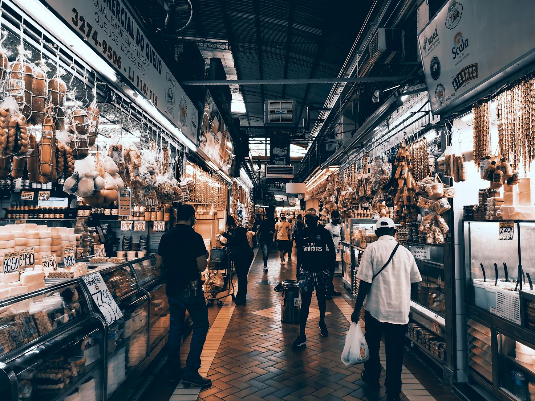 A bustling indoor market aisle filled with diverse shops and people shopping.