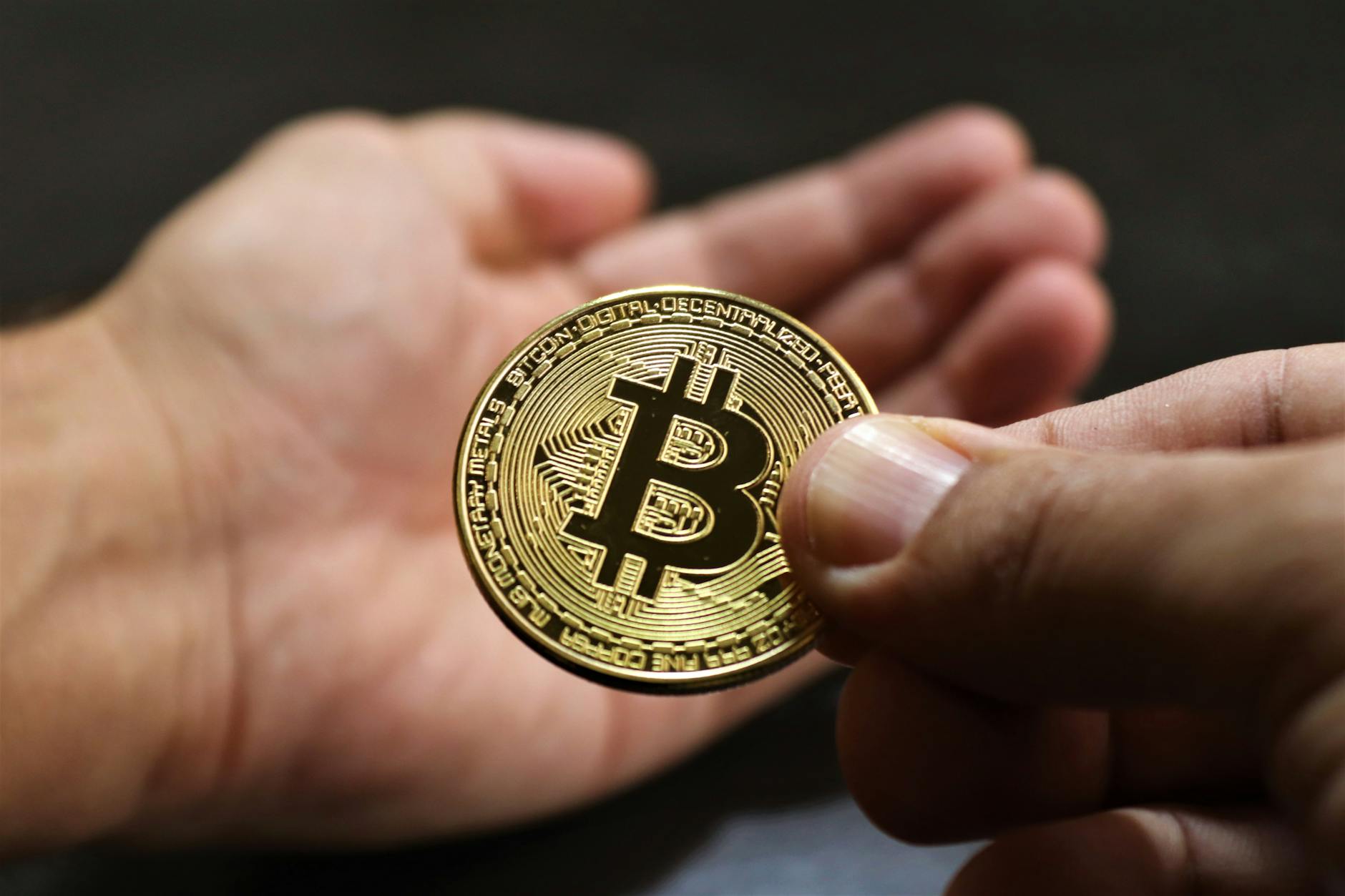 Close-up image showing hands exchanging a Bitcoin coin, symbolizing cryptocurrency transactions.