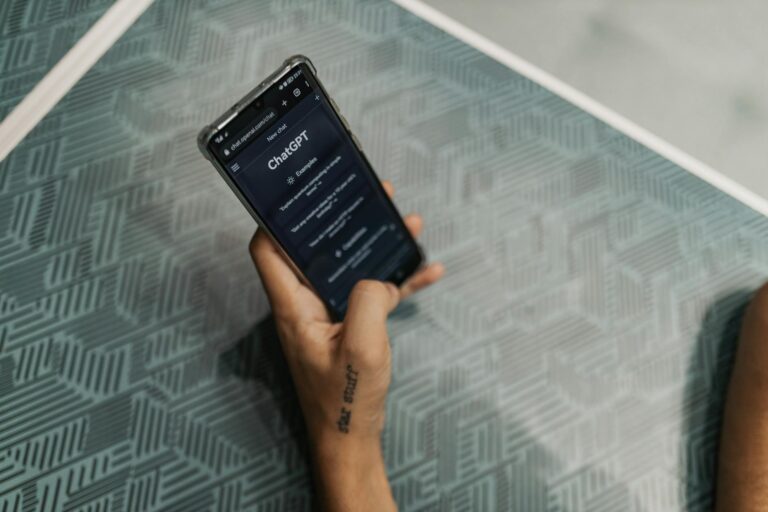 Close-up of a person holding a smartphone displaying the ChatGPT application interface on a patterned table.