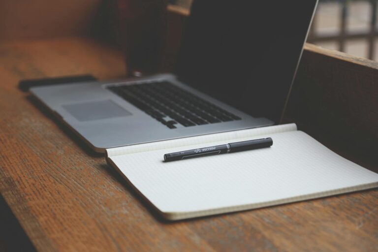 Close-up of a MacBook and notebook on a wooden desk, perfect for productivity.